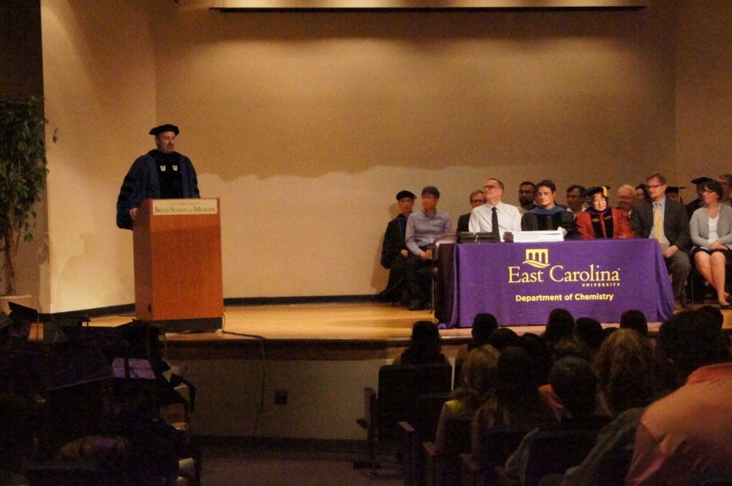 Man at a podium on stage at a graduation ceremony.