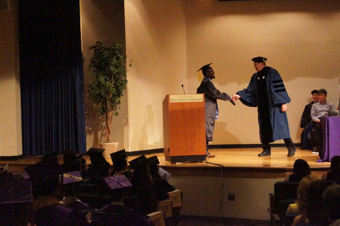 African American man shakes hands with a professor on stage at graduation.