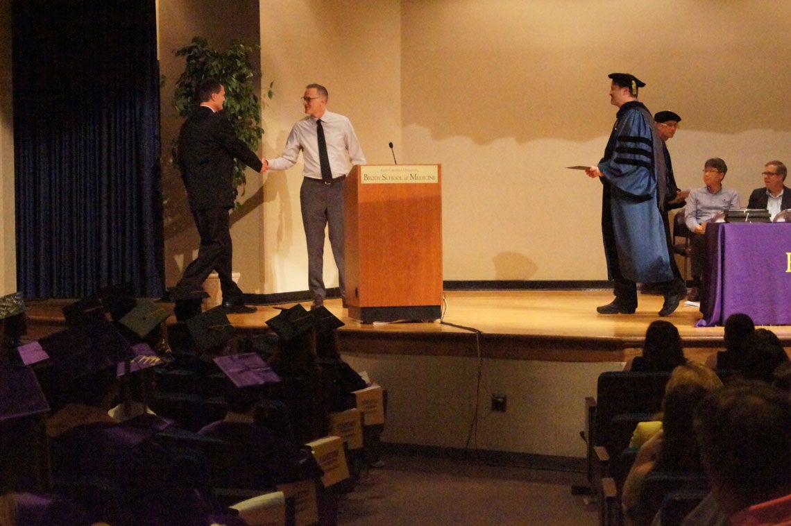 Man shakes hands with professor on stage at a graduation ceremony.