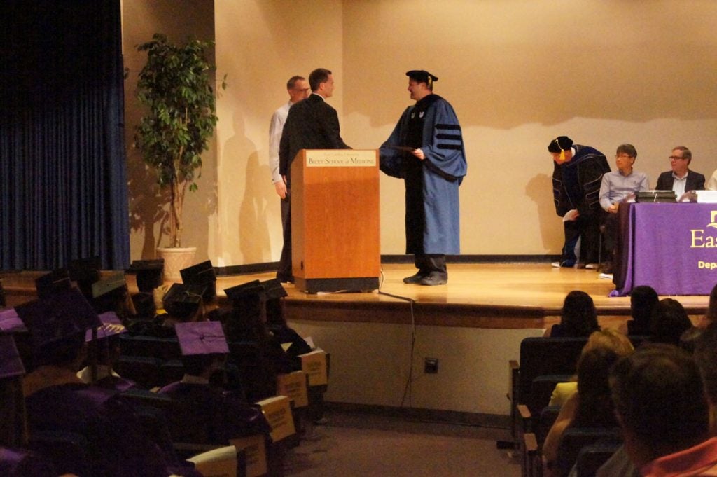 Man shakes hands with professor on stage at a graduation ceremony.