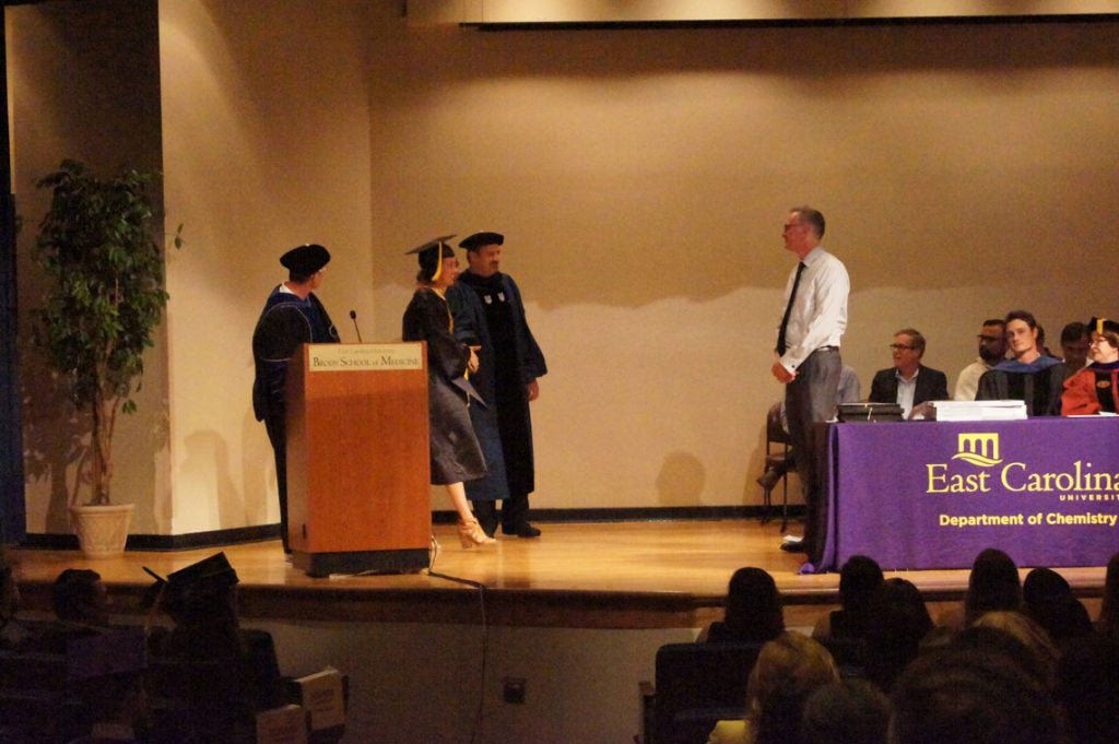 A graduate student walks across the stage at a graduation ceremony.