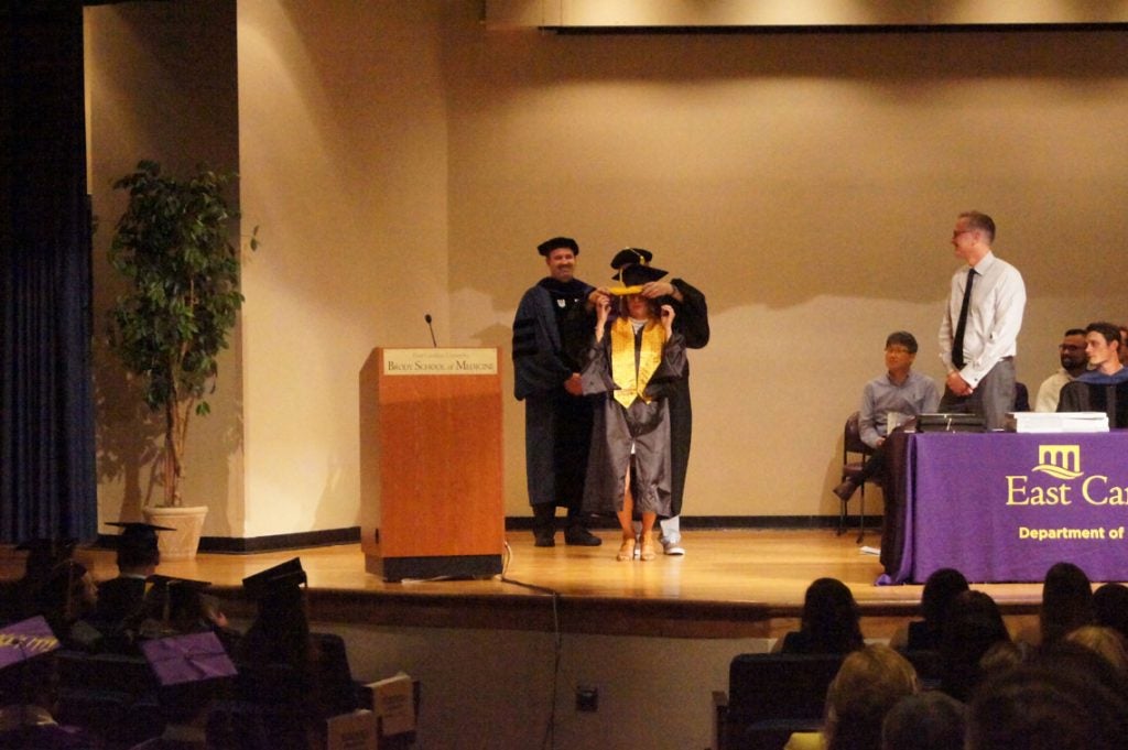 A graduate student receives her hood on stage at a graduation ceremony.