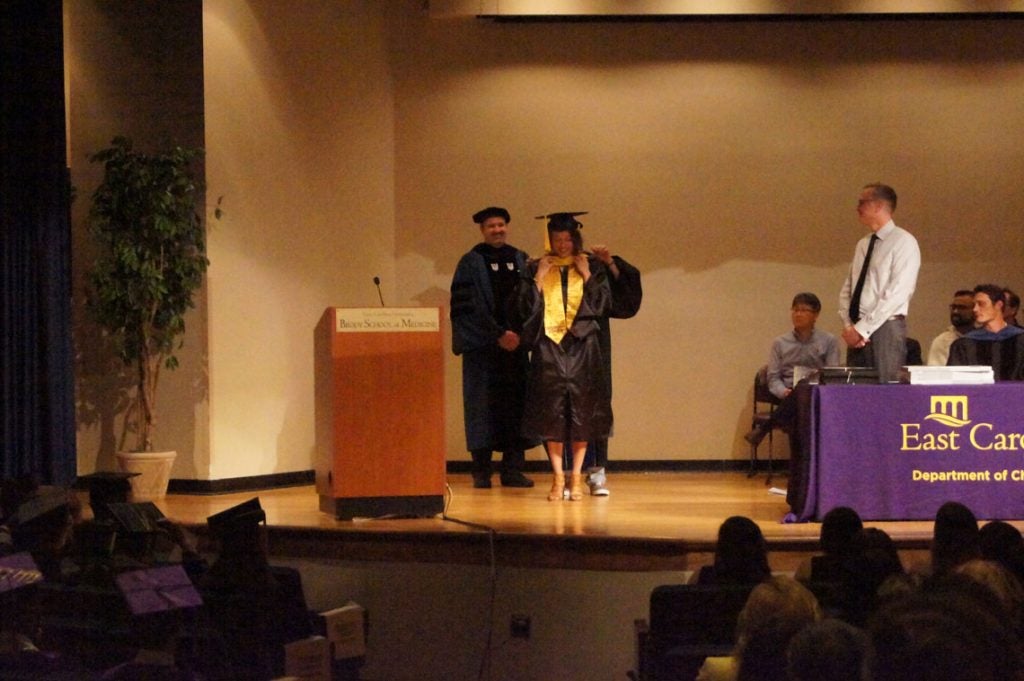 A graduate student receives her hood on stage at a graduation ceremony.