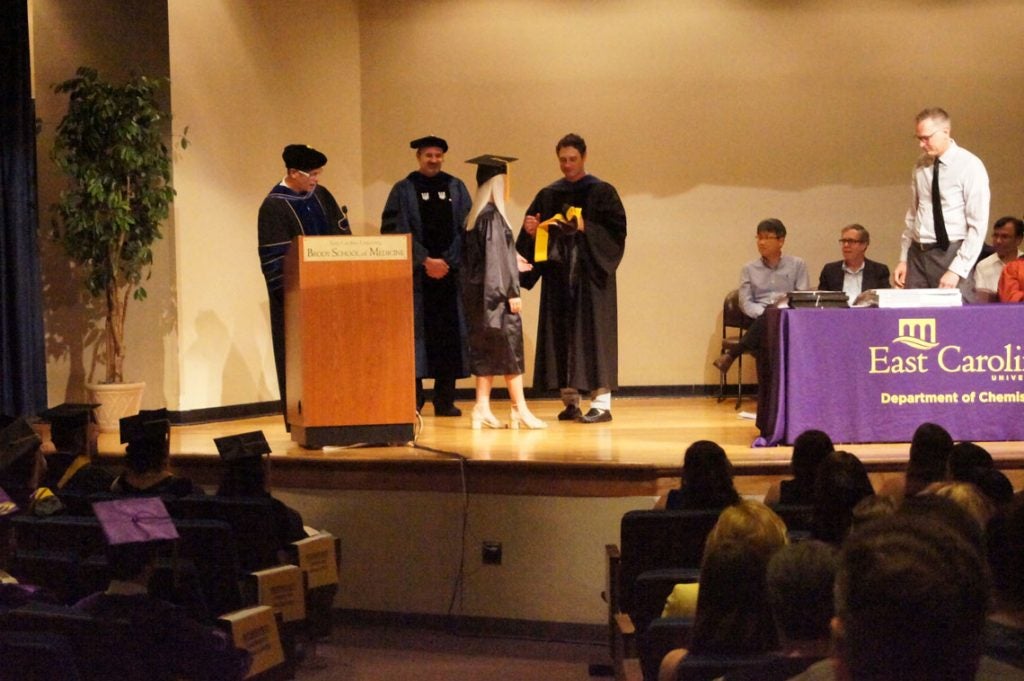 A graduate student receives her hood on stage at a graduation ceremony.