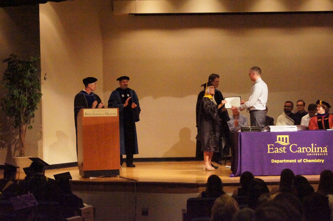 A graduate student receives her degree on stage at a graduation ceremony.