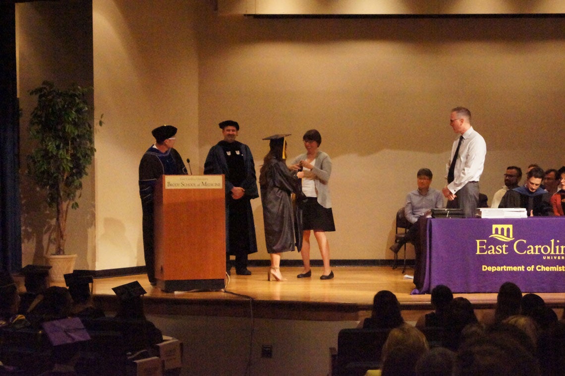 A graduate student receives her hood on stage at a graduation ceremony.