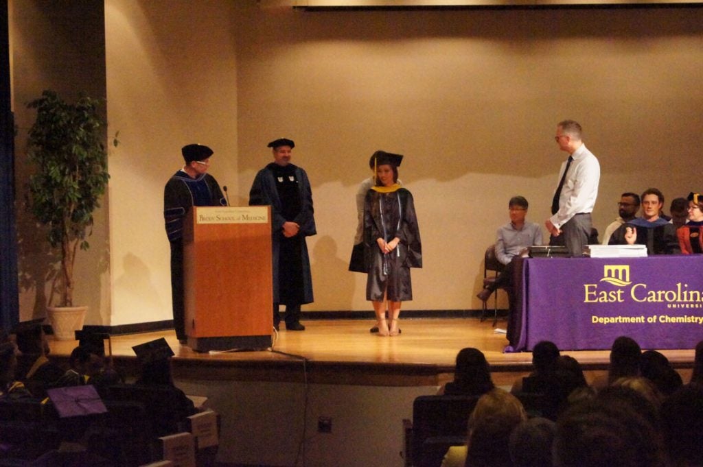 A graduate student receives her hood on stage at a graduation ceremony.