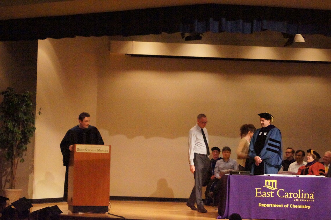 Faculty members on stage at a graduation ceremony.