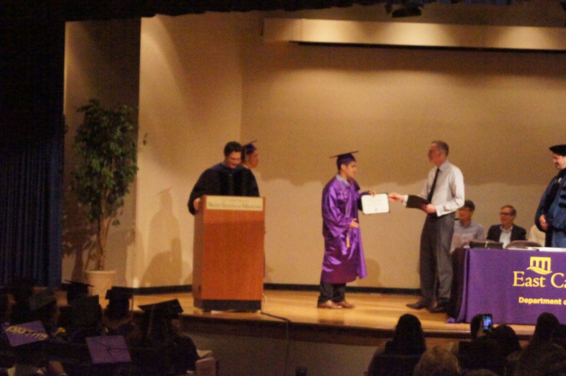 An undergraduate student receives his degree on stage at a graduation ceremony.