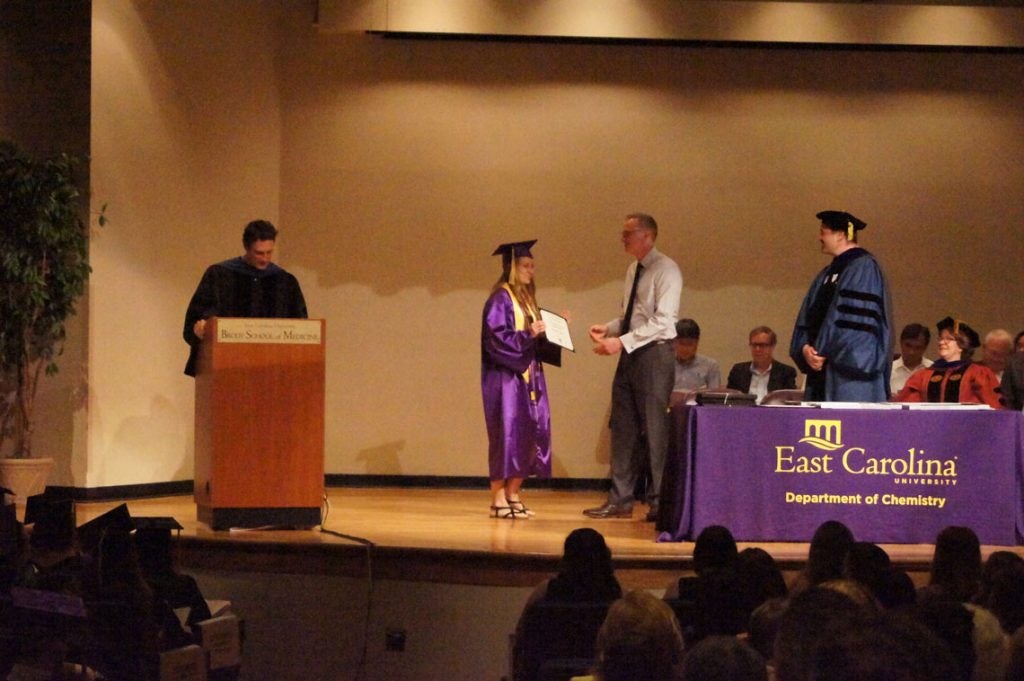 An undergraduate student receives her degree on stage at a graduation ceremony.