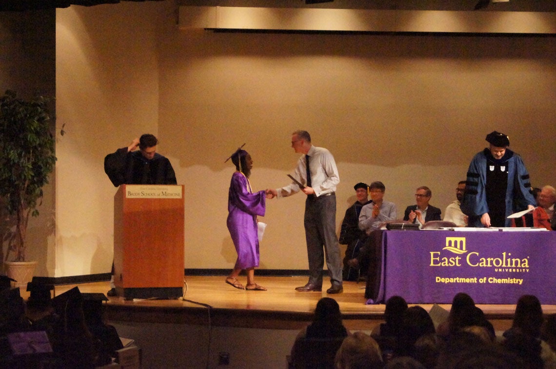 An undergraduate student receives her degree on stage at a graduation ceremony.