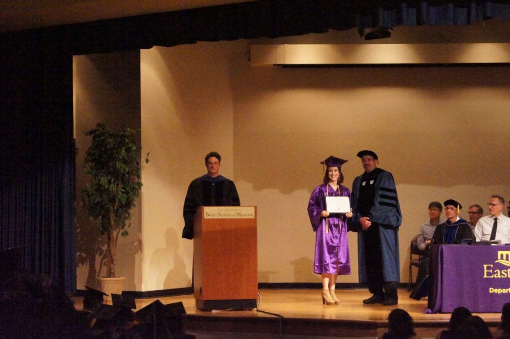 Undergraduate student receives her degree on stage at a graduation ceremony.