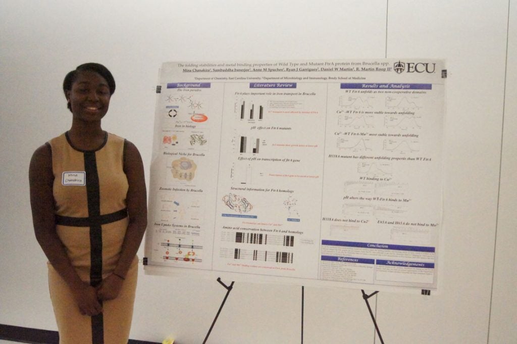 Woman standing next to poster about The folding stabilities and metal binding properties of Wild Type and Mutant FtrA protein from Brucella spp.