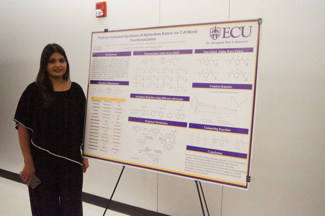 Student standing with poster about Platinum Catalyzed Synthesis of Alpha-Keto Esters via C-H Bond Functionalization.