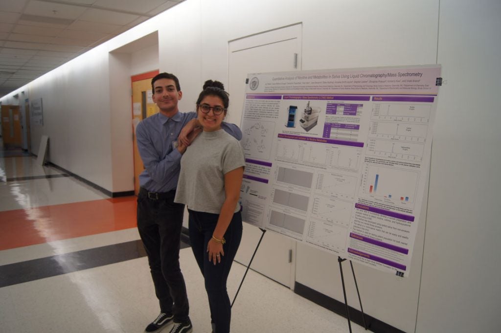 Two students standing next to a poster in a hallway.