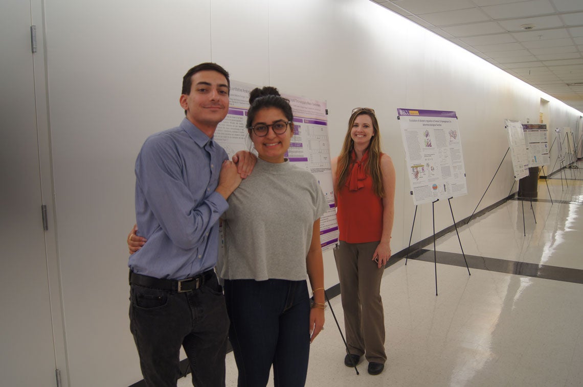 Three students standing next to a poster in a hallway.