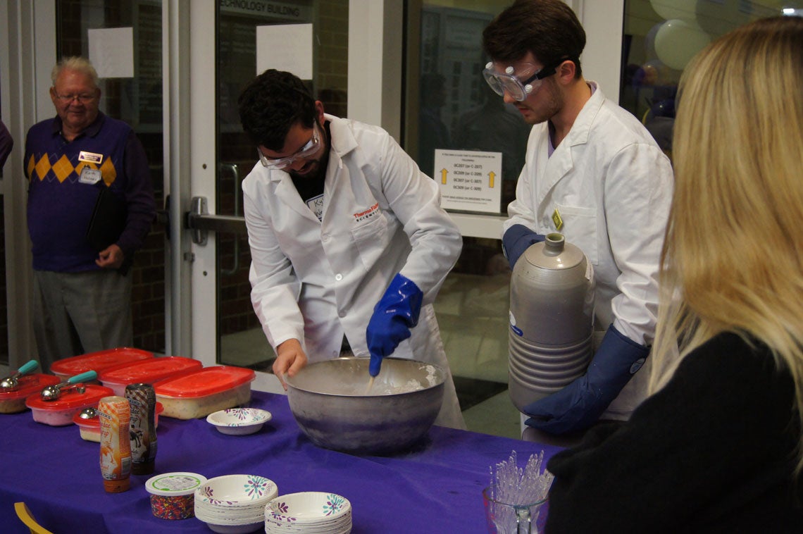 Two men in lab coats and goggles making ice cream with liquid nitrogen.