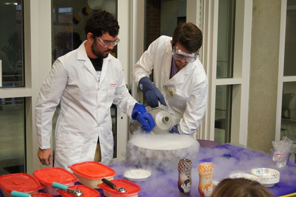 Two men in lab coats making ice cream with liquid nitrogen.